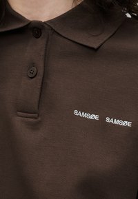 Barna galléros poló két sötét gombbal és fehér „SAMSØE SAMSØE” logóval hímzve a mellrészen.