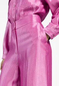 Roze satijnen overhemd en hoge taillebroek, met een zachte textuur, grote knopen en een brede riem.
