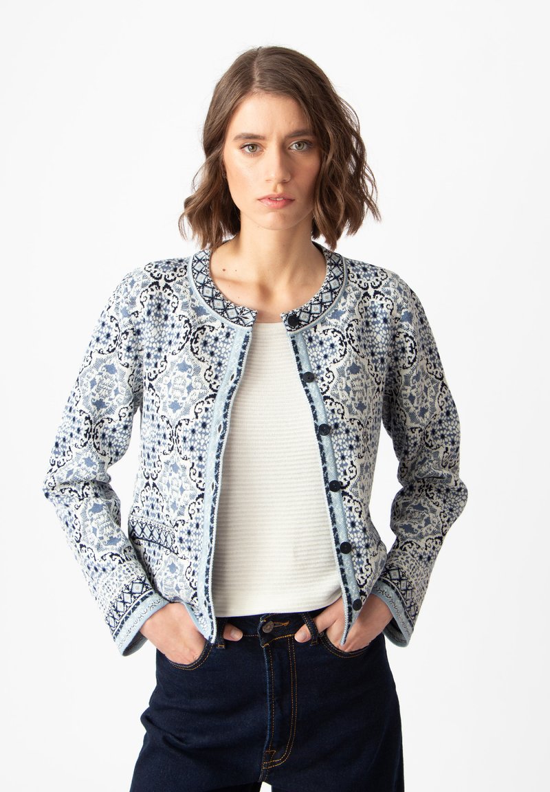 Mėlyna raštuota striukė su sudėtingais dizainais, apvaliu iškirpimu ir mygtukų užsegimu. Nešiojama virš šviesaus marškinėlio ir derinama su tamsiomis džinsinėmis kelnėmis.