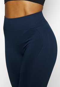 Leggings a vita alta di colore blu navy con una texture liscia e dettagli a coste sottili lungo i lati, progettati per comfort e flessibilità.