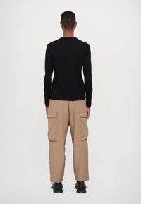 Černá dlouhá rukávová košile, béžové cargo kalhoty s bočními kapsami a černé boty. Jednoduchý design, neutrální barvy a volný střih.