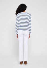 Vit långärmad skjorta med blå horisontella ränder, i kombination med vita utsvängda byxor. Outfits har en avslappnad passform och enkel design.