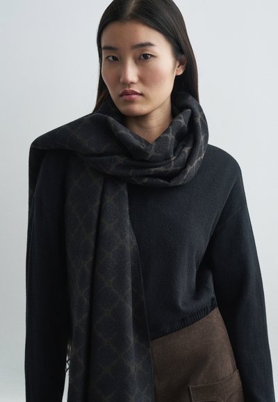 Écharpe en tricot foncé avec un motif géométrique drapée autour du cou. L'écharpe présente une texture douce et un mélange de teintes sombres.