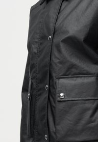 Μαύρο σακάκι στο μπροστινό μέρος με κουμπιά τύπου snap, τσέπη με φερμουάρ και τσέπη με καπάκι που κλείνει με ασ ημένιο snap.