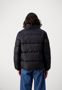 Veste matelassée noire avec un col montant et un design matelassé. Comprend des manches longues et des poignets côtes, associée à un jean en denim bleu clair.