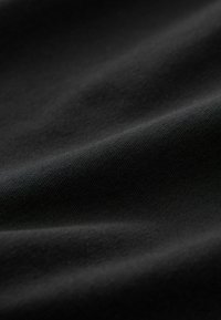 Primo piano di tessuto nero liscio che mostra una fine trama a maglia e pieghe delicate.