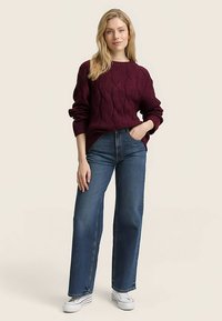 Burgundia punane soonikkoes kampsun, millel on pikad varrukad, kombineeritud kõrge vöökohtade ja sirge säärega siniste teksade ning valgete tossudega. Lihtne ja tekstuuriga disain.