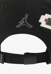 Svart caps med brodert Jumpman-logo og detaljert lapp. Har en strukturert design, justerbar stropp og teksturert stoff.