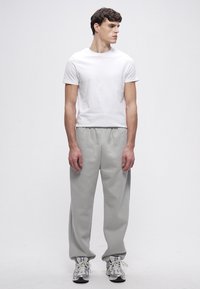 Tricou alb cu mâneci scurte, asortat cu pantaloni de trening gri deschis cu talie elastică, purtat cu adidași de culoare deschisă.