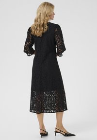 Black lace dress with elbow-length sleeves, a mid-length silhouette, and a floral pattern. Features a subtle back vent and sheer texture.