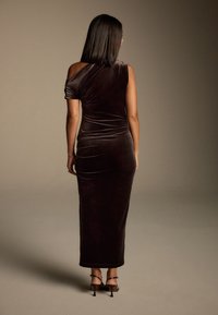 Brūns samts, kleita ar vienu plecu, pieguļošs siluets, līdz ceļiem garums un sānu šķēlums. Valkāta ar sajūga augstpapēžu sandālēm.