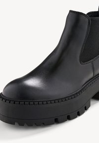 Bottine noire en cuir avec semelle épaisse à crampons et panneau latéral élastique pour un enfilage facile.