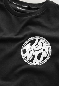 Musta AllSaints T-paita, jossa on pyöreä valkoinen logo, jossa on tyylitelty "ALLSAINTS" -teksti ja "London" suunnittelussa kaula-aukon lähellä.