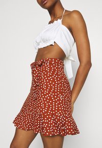 Falda marrón con lunares y dobladillo con volantes, con un lazo en la cintura; combinada con un top corto blanco con detalles de tela fruncida.