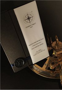 Zwarte map met reliëfontwerp van een kompas, waarin een witte productinzet voor oogpleisters zit, met zwart tekst en een blauwe striksluiting.