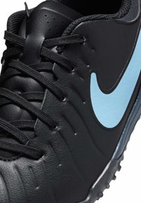 Svart syntetisk fotbollssko med texturerad yta, utrustad med en ljusblå Nike-logotyp, svarta snören och gummistöd med dobbar.