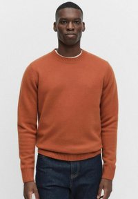 Terrakottafärgad crew neck-tröja, stickad, med ribbade muddar och nederkant, mjuk textur, i kombination med mörka jeans.