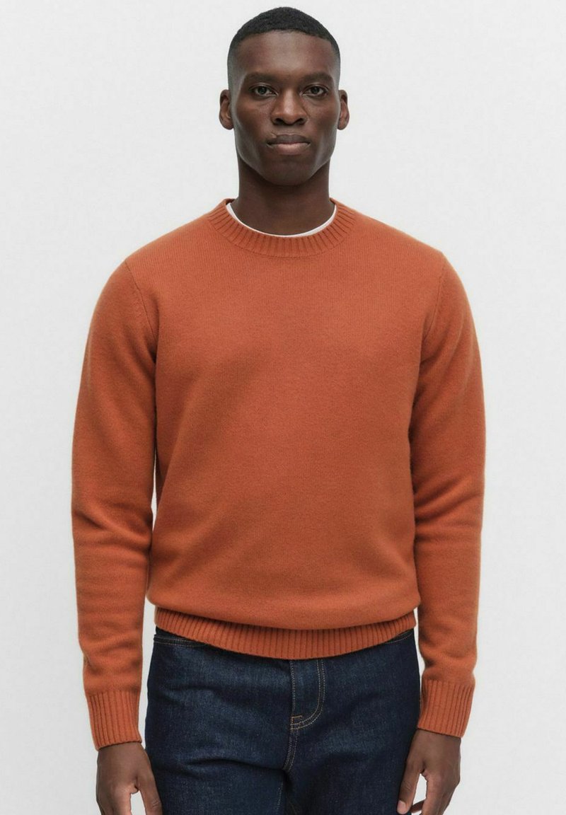 Terrakottafärgad crew neck-tröja, stickad, med ribbade muddar och nederkant, mjuk textur, i kombination med mörka jeans.