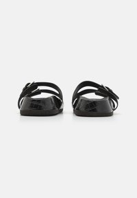 Sorte sandaler med et teksturert krokodillemønster, åpen bakdesign, justerbar spenne og flat såle. Glatt materiale med minimal detaljering.