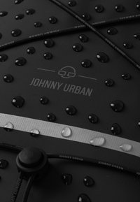 Čierny materiál s kvapkami vody, strieborným pruhom a šnúrkou na stiahnutie s brandingom "JOHNNY URBAN". Viditeľný textúrovaný vzor povrchu.