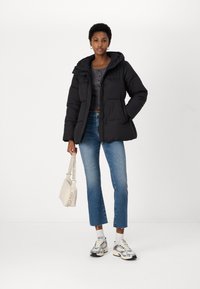 Black puffer jacket with a hood, short length, diamond pattern, button closures, paired with light blue straight-leg jeans and sneakers.