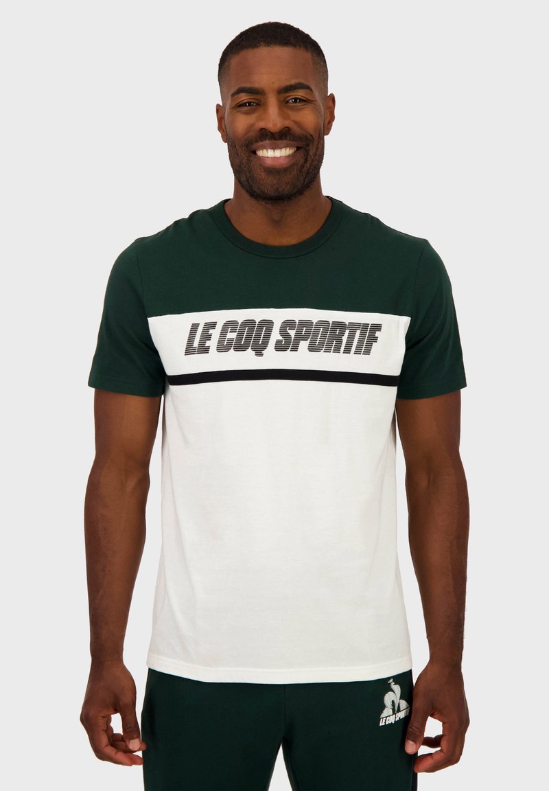 Camiseta de manga corta en verde y blanco con un audaz logo negro. Cuello redondo, material de algodón y diseño en bloques de color contrastantes.
