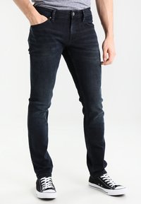 Mörka denimjeans med slim fit, som har framfickor, dragkedja och synlig sömnad. Kombinerat med svarta och vita sneakers.