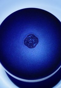 Contenitore tondo blu con finitura opaca e design floreale in rilievo al centro, con un bordo liscio e pulito.