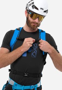 Schwarzes technisches Hemd mit blauen Akzenten, verstellbaren Trägern und einem Gurtzeug. Zubehör umfasst einen weißen Helm und eine verspiegelte Sonnenbrille.