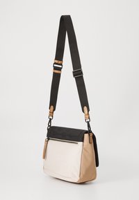 Borsa a tracolla con parte superiore nera e sezione inferiore color crema, dotata di una cerniera, dettagli in pelle beige e tracolla regolabile.