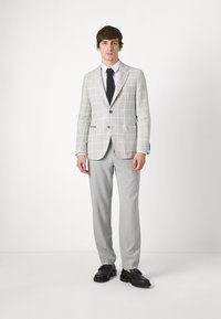 Lichtgrijze geblokte blazer met notch lapels, grijze pantalon en zwarte instapschoenen. Textuurstof met subtiel ruitpatroon.