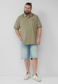 Olijf groene polo shirt met marineblauwe strepen op de kraag, gecombineerd met lichtblauwe denim shorts. Witte sneakers maken de outfit compleet.