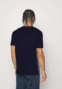 Námořnické modré tričko s krátkým rukávem a kulatým výstřihem, zdobené kontrastními bílými bočními pruhy a logem značky na okrajích.