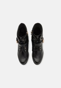 Botas de tobillo de cuero negro con herrajes dorados, cordones en la parte frontal y cremallera lateral. Textura suave con un diseño de punta redonda.
