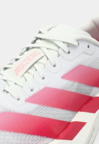 Scarpa da ginnastica bianca con strisce rosa, lacci bianchi e un'etichetta con la scritta "ADIZERO" vicino alla linguetta su uno sfondo chiaro.