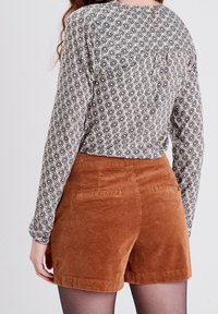 Dlouhý rukáv tričko v černo-bílém geometrickém potisku s kulatým výstřihem, spárováno s hnědými kordurovými šortkami s zadními kapsami.