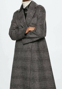 Manteau à carreaux gris avec un design structuré, présentant un col cranté, des manches longues et une coupe ample qui tombe jusqu'à mi-mollet.