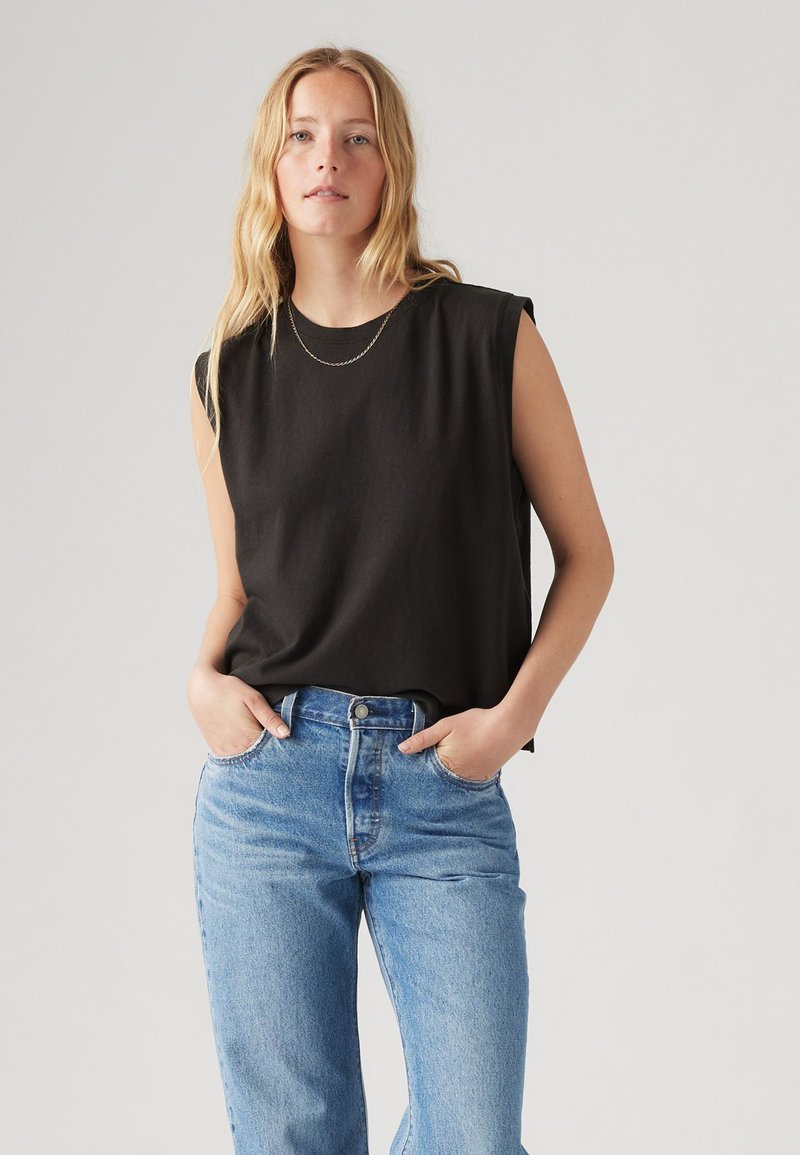 Svart ärmlös topp med avslappnad passform och rundad halsringning, kombinerad med ljusblå högmidjade jeans. Slät bomullstextur.