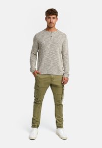 Szary, strukturalny, długi rękaw koszula z trzema guzikami, w połączeniu z oliwkowymi spodniami typu cargo z wieloma kieszeniami oraz białymi sneakersami.