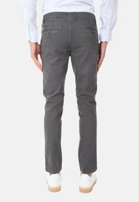 Chinos grigi slim-fit con una texture liscia, dotati di tasche posteriori con bottoni e una vita standard, indossati con sneakers bianche.