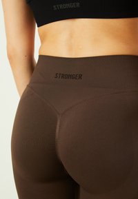 Barna bordás leggings magas derékkal, a derékrészen fekete "STRONGER" felirattal, kiemelve a feszes szabást.