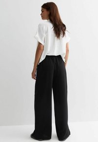 Witte oversized top met opgerolde mouwen, gecombineerd met zwarte wijde broek met elastische tailleband en zachte textuur.