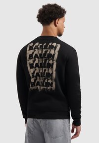 Zwarte sweatshirt met een grote, getextureerde beige "BALLIN" print op de achterkant. Geribbelde manchetten en onderkant, ontspannen pasvorm, zachte katoenen stof.