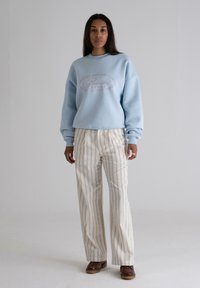 Sudadera de gran tamaño en azul claro con un logo gráfico y pantalones de pierna ancha a rayas color crema. Zapatos marrones completan el conjunto.