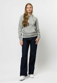 Ljusgrå hoodie med framficka och dragsko, ihop med mörkblå utsvängda jeans och vita sneakers. Enkla egenskaper och avslappnad passform.