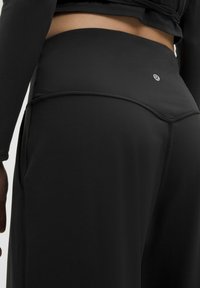 Leggings de sport noirs taille haute en matériau lisse et extensible, avec un logo discret, des coutures plates et une coupe ajustée.