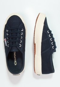 Marineblå kanvas sneakers med hvite lisser og gummisåle. Har merkevarelogo, teksturert overdel og en kontrastfarget brun yttersåle. Rund tådesign.