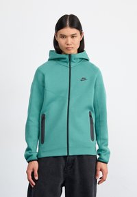 Teal Nike hoodie with a full zip, adjustable hood, black logo, and two zippered pockets on the front. Smooth, stretchy fabric, fitted design.