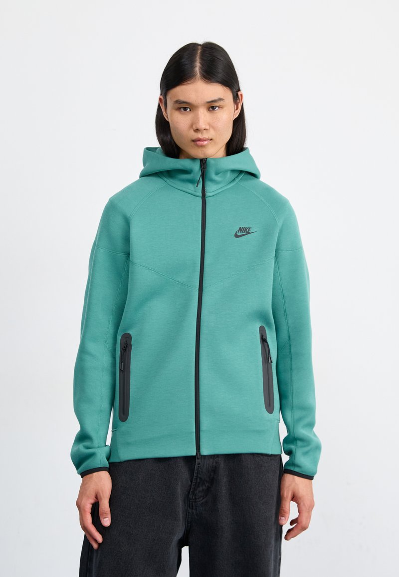 Teal Nike hoodie with a full zip, adjustable hood, black logo, and two zippered pockets on the front. Smooth, stretchy fabric, fitted design.