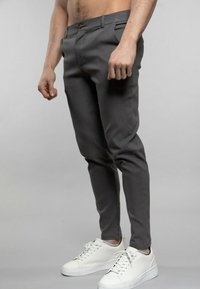 Pantalons gris à coupe slim, avec un devant plat, deux poches latérales et une seule poche arrière. Associés à des baskets blanches.